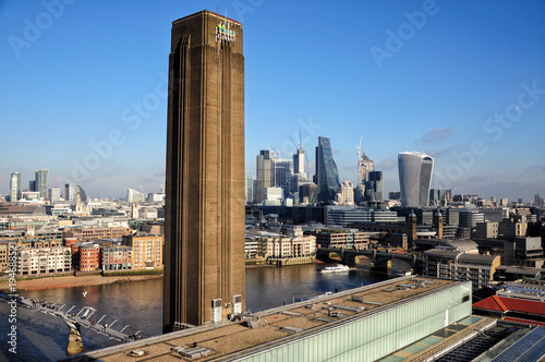 Tate modern famous chimney with the business district of London in the background. Typical brown brick walls building and modern architecture. Clear sky on sunny day photo