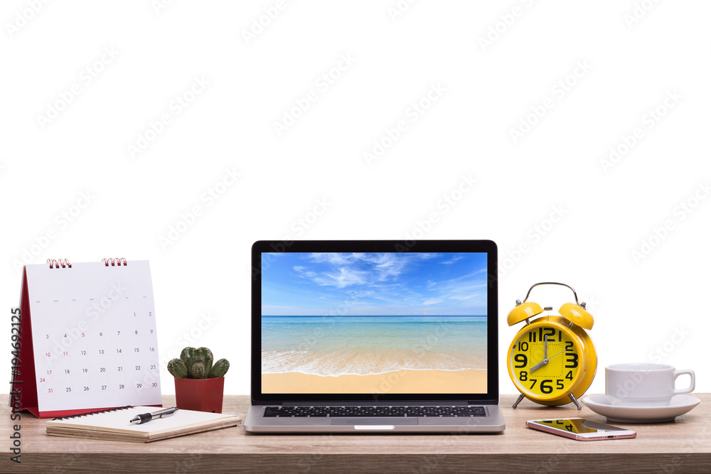Modern laptop computer, Coffee cup, alarm clock, notebook and calendar on wooden table and view of tropical beach. Saved with clipping path. Work and holiday concept