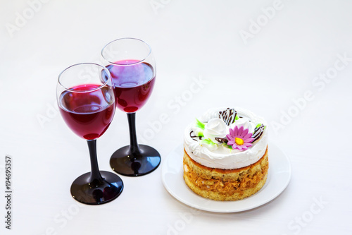 Two elegant glasses of red wine and biscuit cake on a white plate. Festive drinks and dessert for celebration on white background.