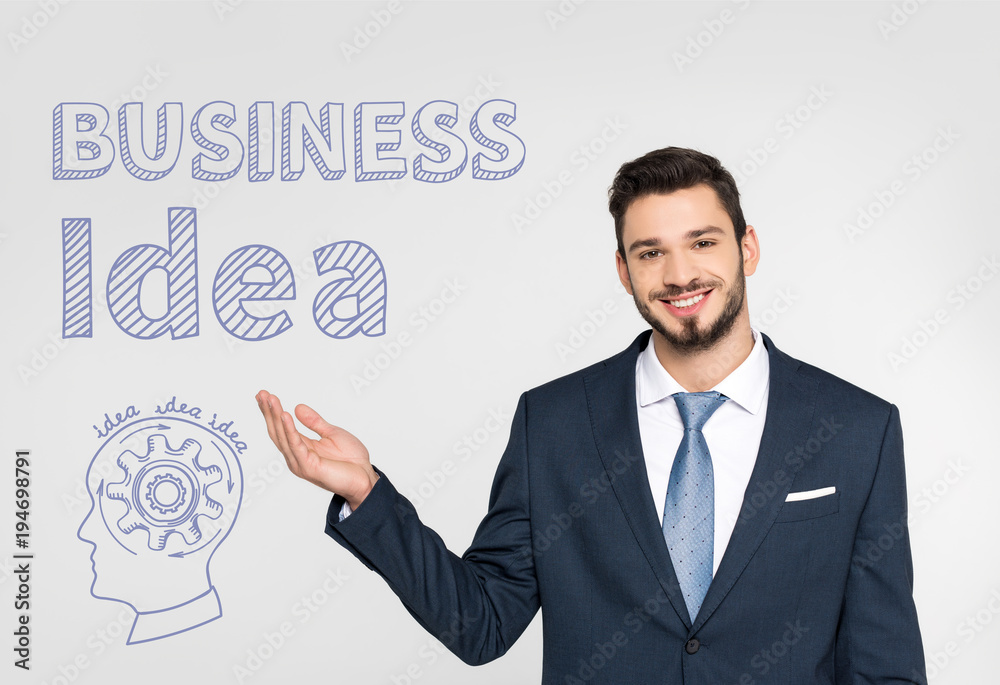 handsome young businessman showing startup icons and smiling at camera isolated on grey handsome young businessman showing startup icons and smiling at camera isolated on grey