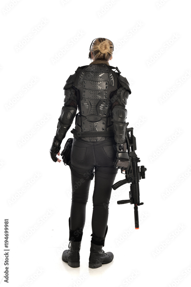 full length portrait of female  soldier wearing black  tactical armour, standing  with back to the camera holding a gun, isolated on white studio background.