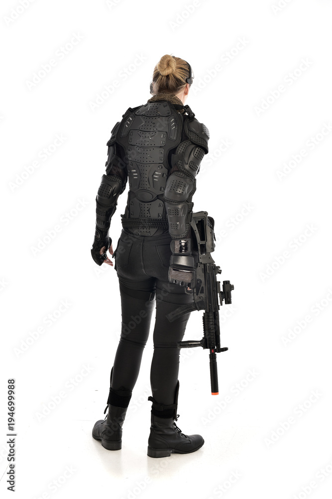 full length portrait of female soldier wearing black tactical armour, standing with back to the camera holding a gun, isolated on white studio background. full length portrait of female soldier wearing black tactical armour, standing with back to the camera holding a gun, isolated on white studio background.
