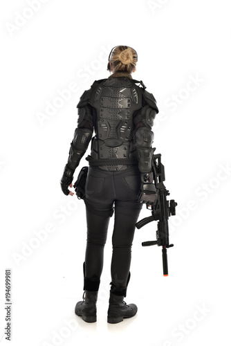 full length portrait of female  soldier wearing black  tactical armour, standing  with back to the camera holding a gun, isolated on white studio background.