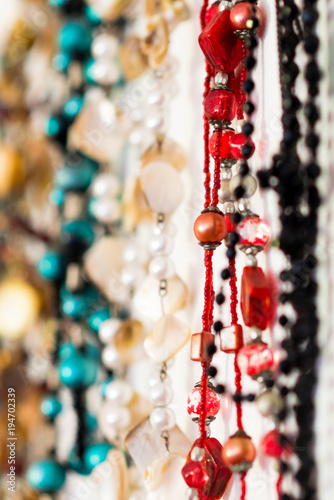 An abstract closeup of colourful beaded necklaces hanging in a row against a white background, with negative white space to the right of the necklaces