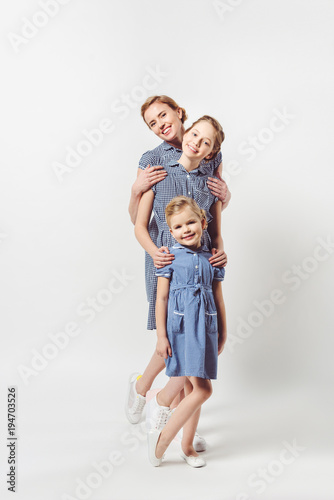 smiling mother and daughters in similar dresses isolated on grey