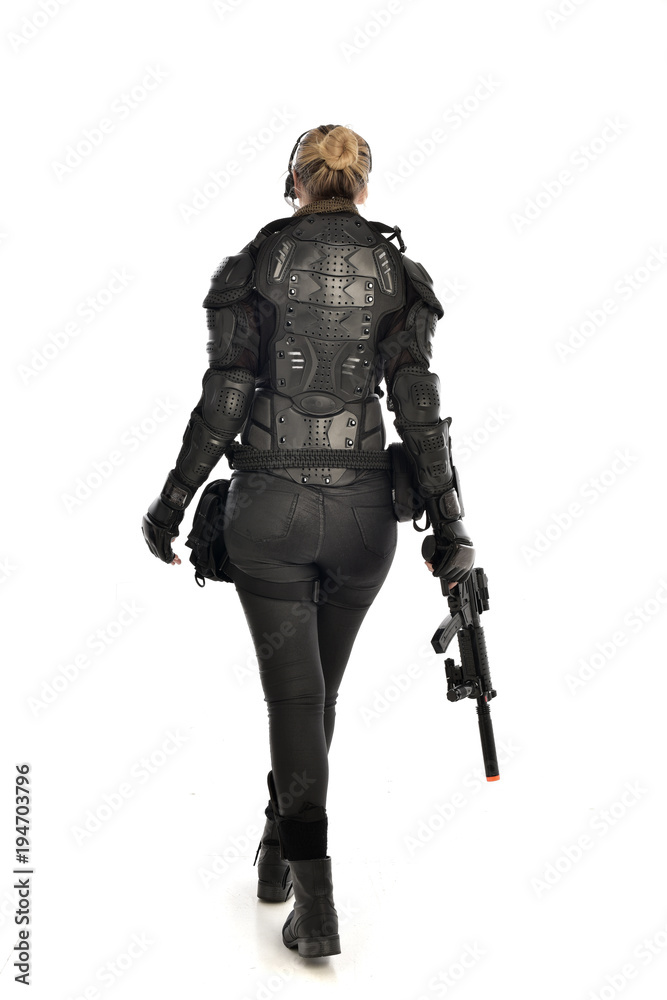 full length portrait of female soldier wearing black tactical armour, standing with back to the camera holding a gun, isolated on white studio background. full length portrait of female soldier wearing black tactical armour, standing with back to the camera holding a gun, isolated on white studio background.