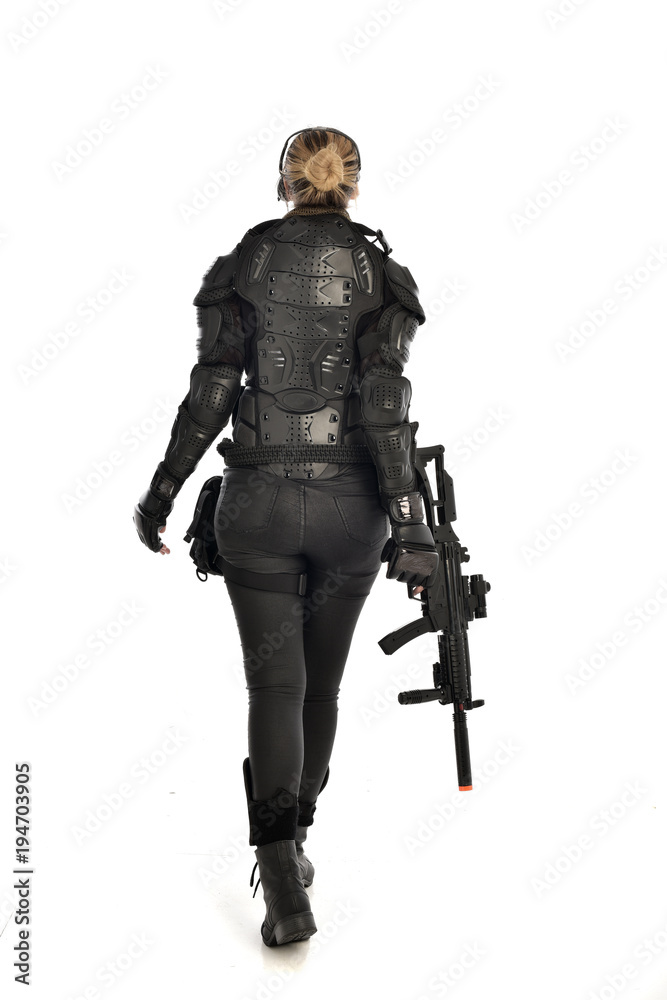 full length portrait of female soldier wearing black tactical armour, standing with back to the camera holding a gun, isolated on white studio background. full length portrait of female soldier wearing black tactical armour, standing with back to the camera holding a gun, isolated on white studio background.