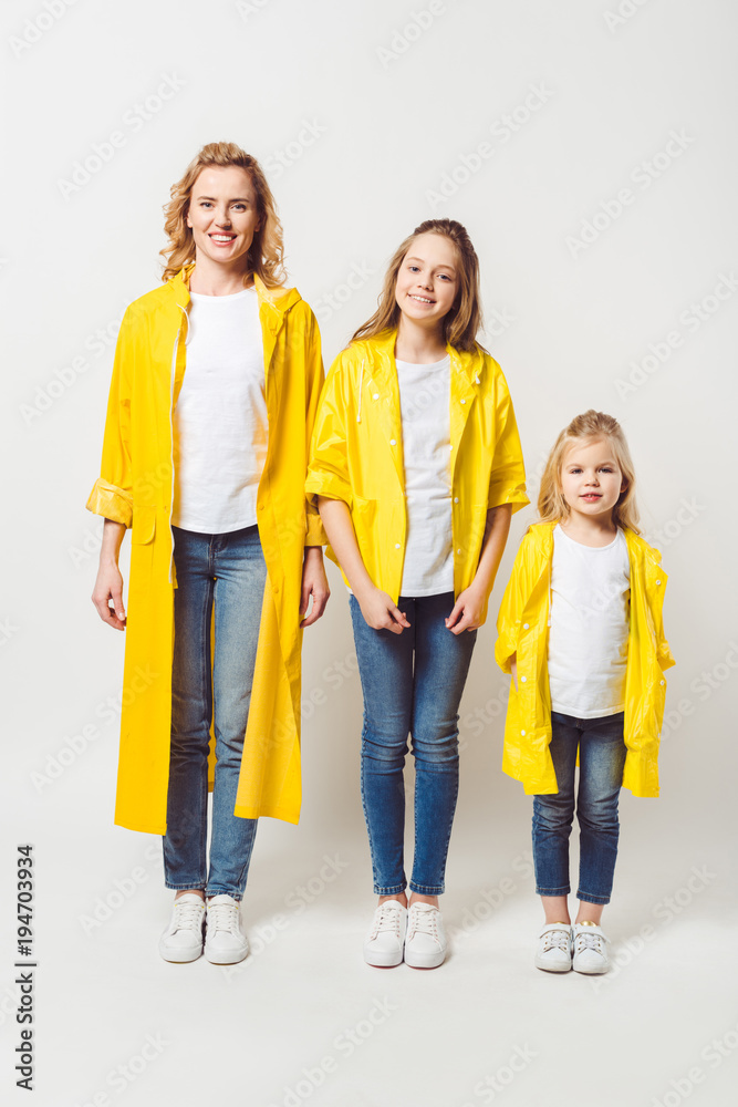 Obraz premium beautiful mother and daughters in yellow raincoats on white