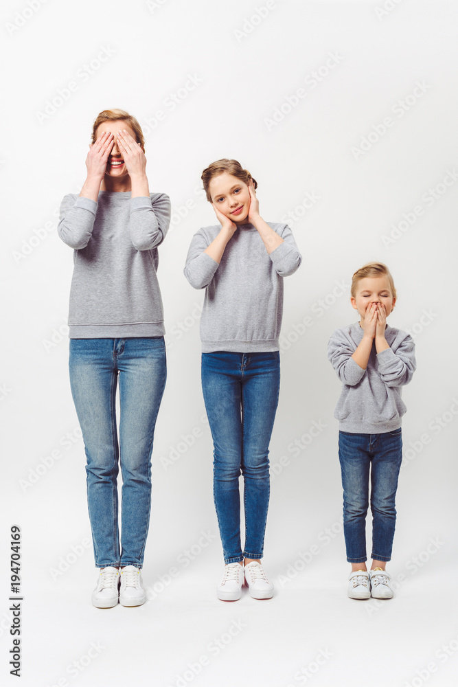 mother and daughters of different generations in similar clothing covering parts of faces isolated on grey mother and daughters of different generations in similar clothing covering parts of faces isolated on grey