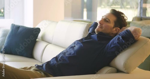 A man relaxes on the sofa at home, hugging a pillow and watching a movie in canvas and smile. Concept of: leisure, relax, tv.