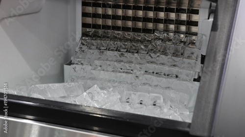 cube ice in ice making machine that door open ; to transform liquid water to solid ice  below zero  degree celsius  ; food and drink industrial background ; close up photo