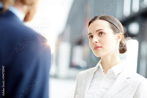 Young confident specialist listening attentively to what her colleague speaking at meeting