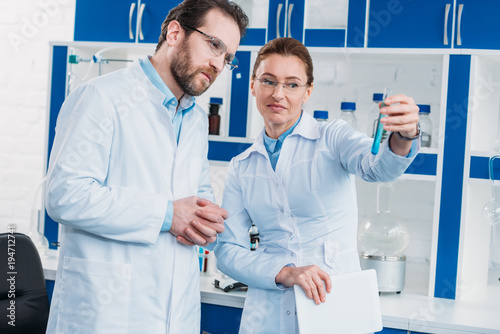 portrait of scientists in eyeglasses looking at tube with reagent in laboratory