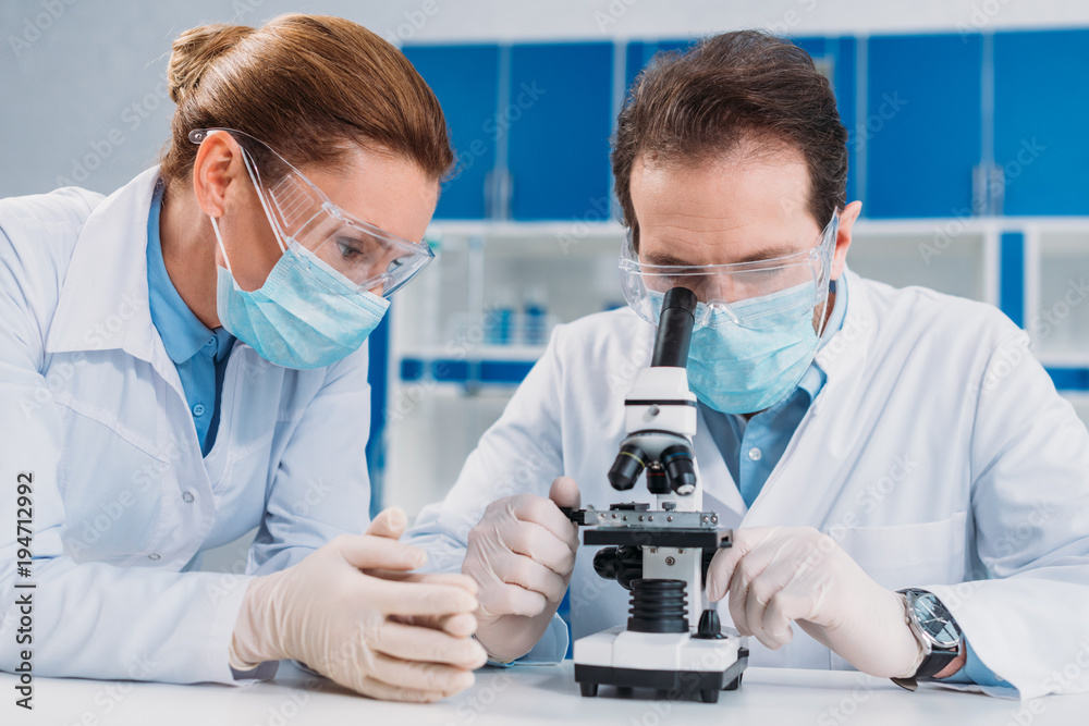 portrait of researchers in medical masks and gloves working with microscope together in lab