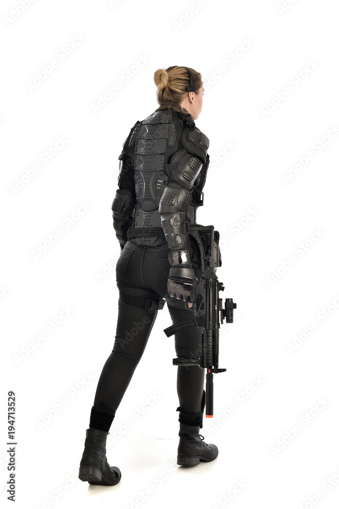 full length portrait of female soldier wearing black tactical armour, standing with back to the camera holding a gun, isolated on white studio background. full length portrait of female soldier wearing black tactical armour, standing with back to the camera holding a gun, isolated on white studio background.