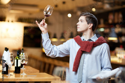 Satisfied young man looking at red glass of wine during a winetasting