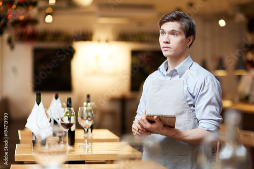 Male waiter standing with notepad and ready to accept the order