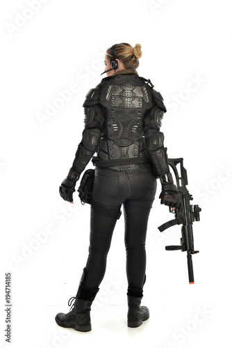 full length portrait of female  soldier wearing black  tactical armour, standing  with back to the camera holding a gun, isolated on white studio background.