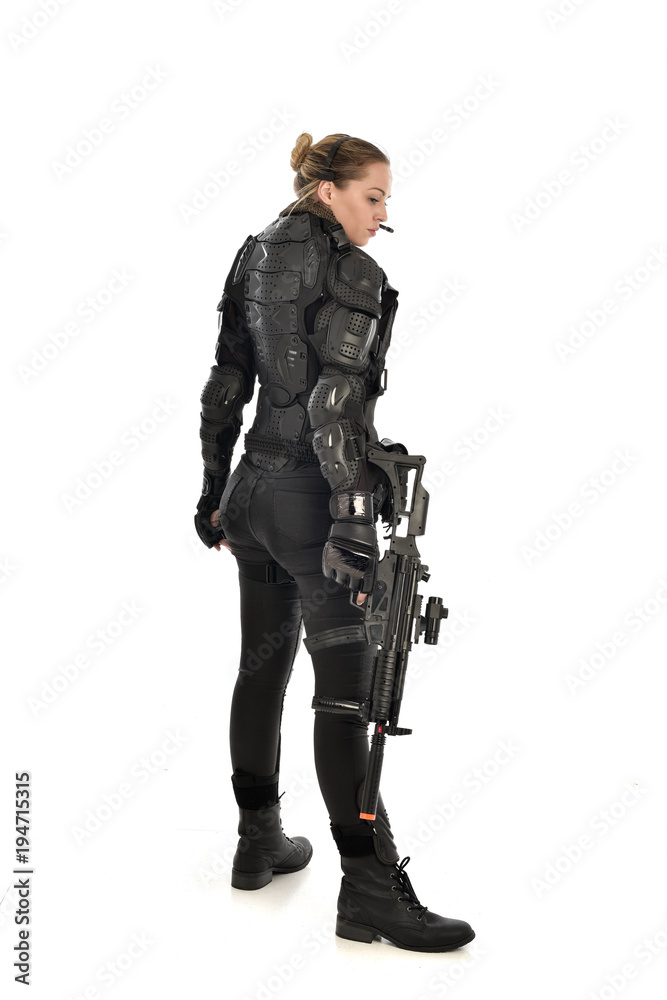 full length portrait of female soldier wearing black tactical armour, standing with back to the camera holding a gun, isolated on white studio background. full length portrait of female soldier wearing black tactical armour, standing with back to the camera holding a gun, isolated on white studio background.