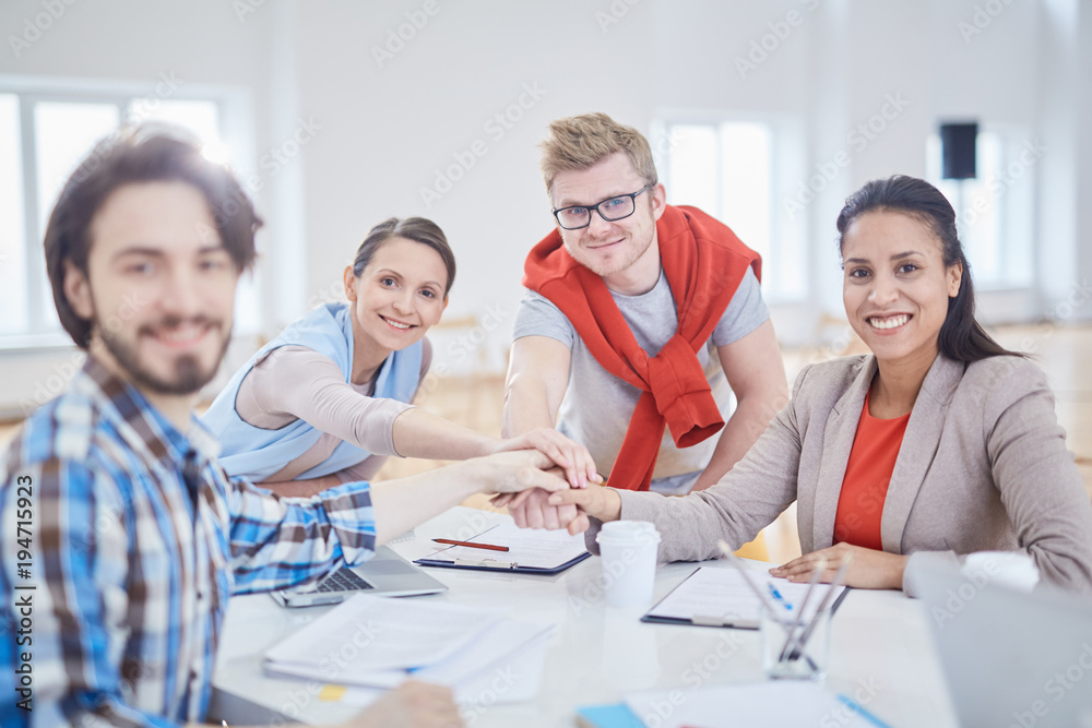 Four young successful employees making pile of hands over desk with papers at meeting Four young successful employees making pile of hands over desk with papers at meeting