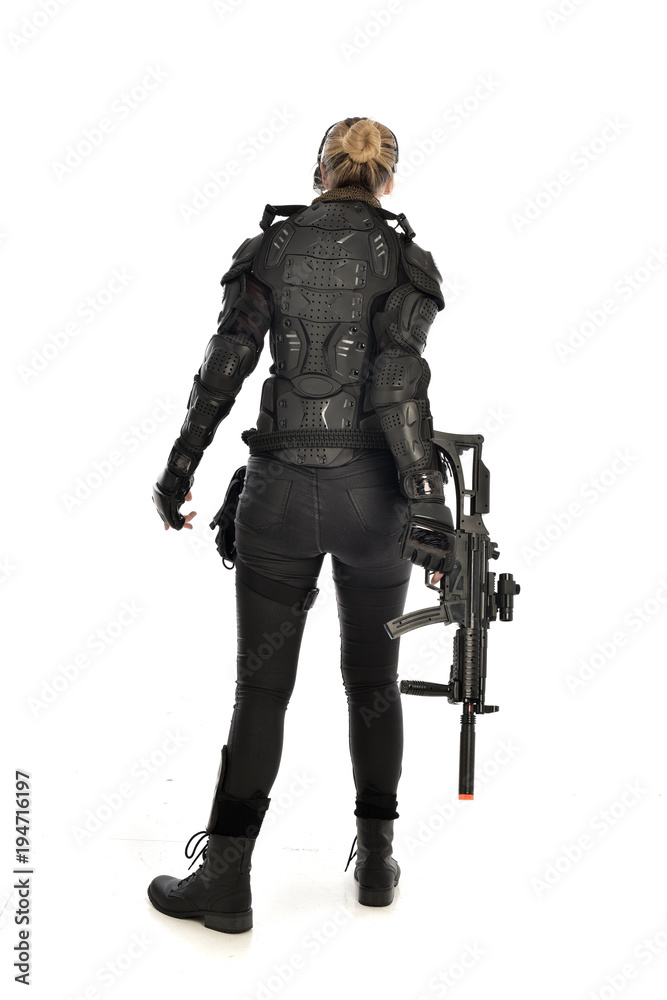 full length portrait of female soldier wearing black tactical armour, standing with back to the camera holding a gun, isolated on white studio background. full length portrait of female soldier wearing black tactical armour, standing with back to the camera holding a gun, isolated on white studio background.