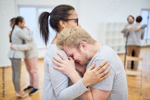 Young troubled man crying on shoulder of his groupmate while she comforting him