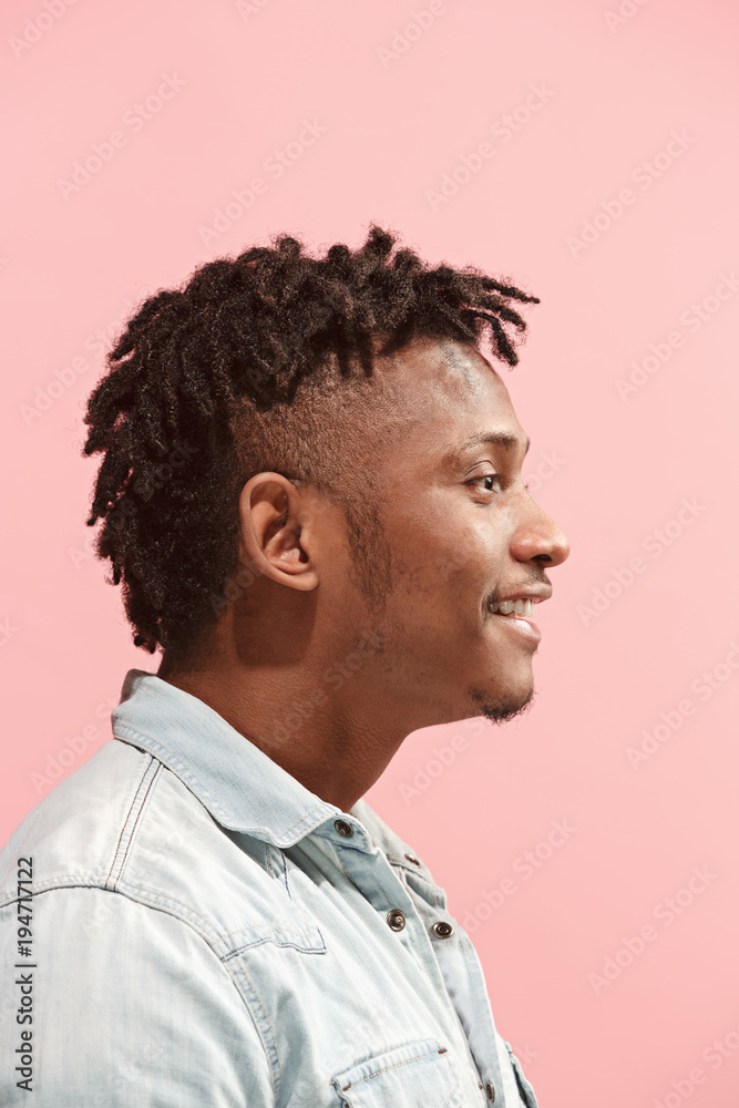 The happy business Afro-American man standing and smiling against pink background. Profile view. The happy business Afro-American man standing and smiling against pink background. Profile view.