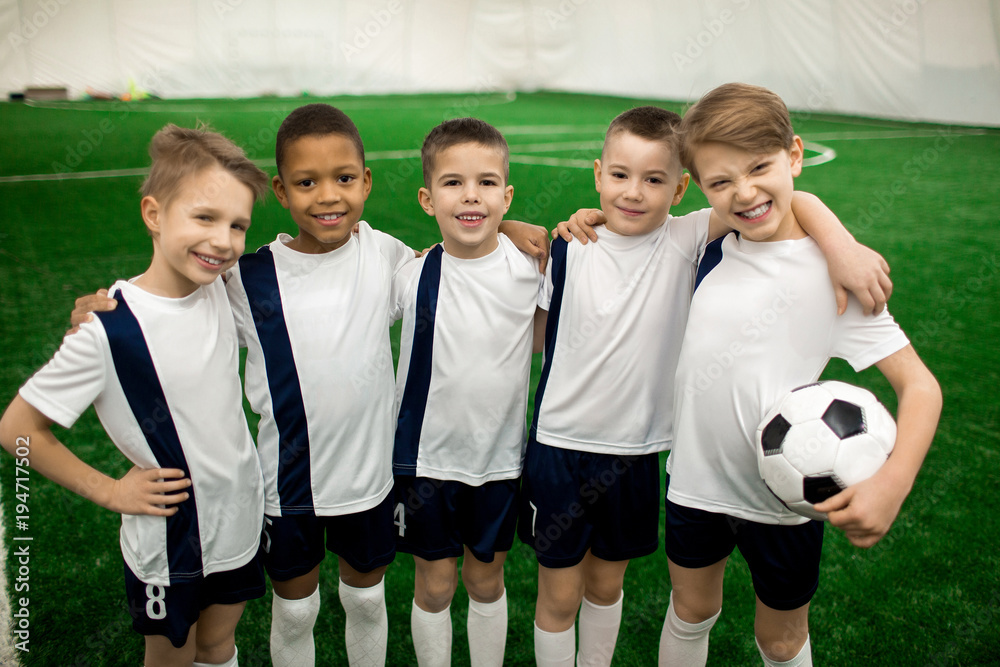 Happy football team of five successful members in uniform looking at camera on pitch Happy football team of five successful members in uniform looking at camera on pitch