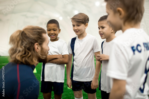 Sports trainer consulting his football team of four boys before new game or competition