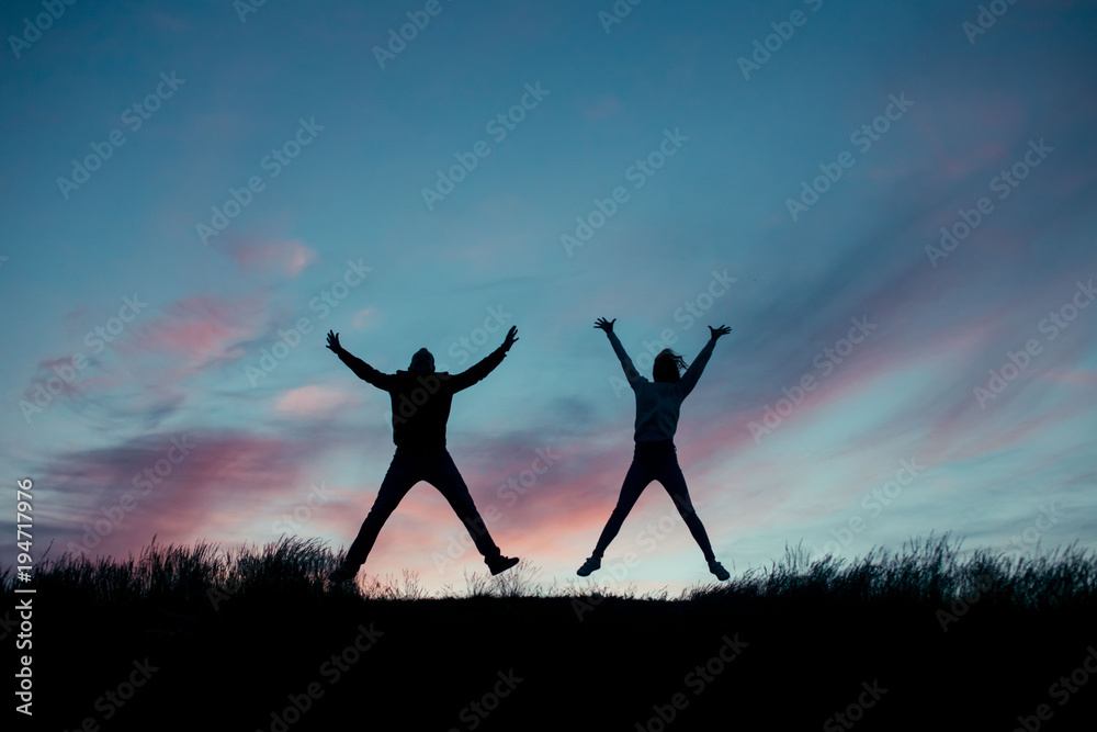 Silhouette of a loving couple. Jumping from happiness couple on top of a hill on a background of the setting sun
