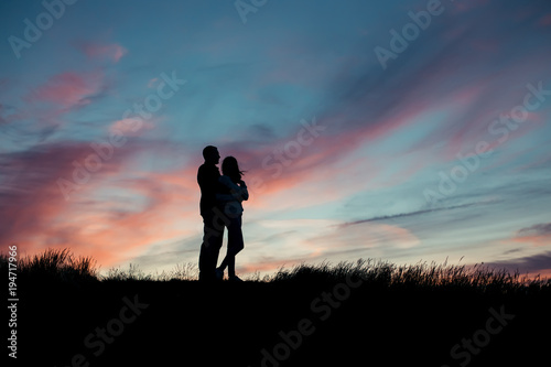Silhouette of a loving couple hugging on a hill top against the backdrop of the setting sun © Maksim Ksenofontov