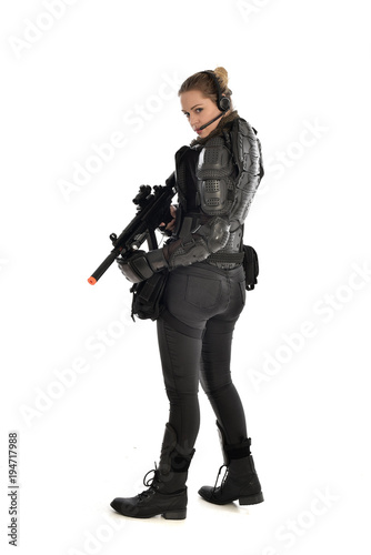 full length portrait of female  soldier wearing black  tactical armour  standing  with back to the camera holding a gun  isolated on white studio background.
