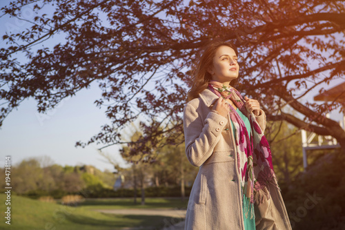 Cute ordinary caucasian brunette woman in casual outfit walking at the nature park. Cold spring  autumn  weather  warm coat on a girl. Sunset. Copy space