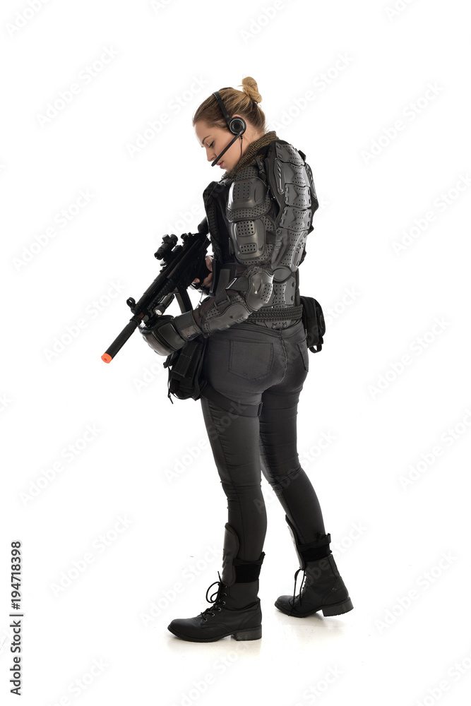 full length portrait of female soldier wearing black tactical armour, standing with back to the camera holding a gun, isolated on white studio background. full length portrait of female soldier wearing black tactical armour, standing with back to the camera holding a gun, isolated on white studio background.