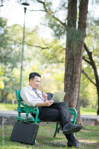 Businessman sitting on the park bench with laptop