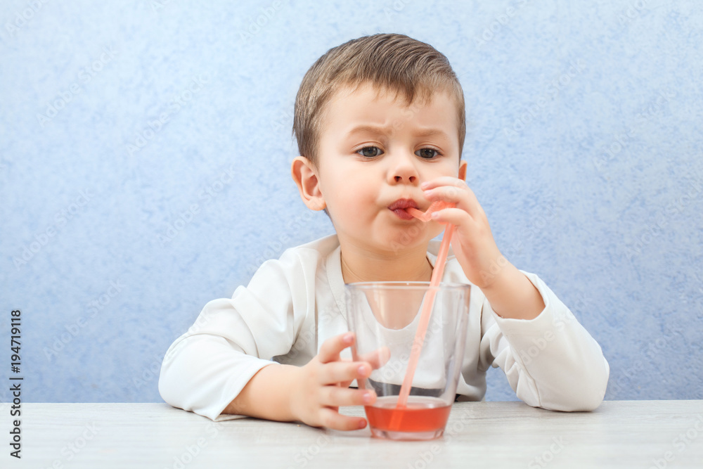 Cute little boy drinking juice on light blue background. Lovely kid drink grape juice. Cute little boy drinking juice on light blue background. Lovely kid drink grape juice.