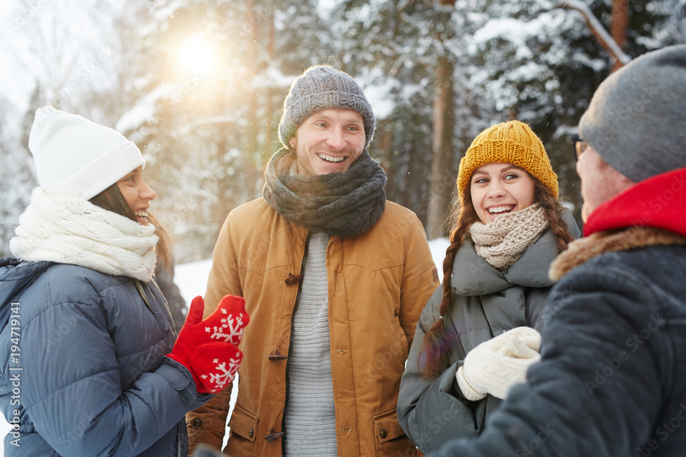 Group of young cheerful friends in winterwear having talk on snowy day in the forest Group of young cheerful friends in winterwear having talk on snowy day in the forest