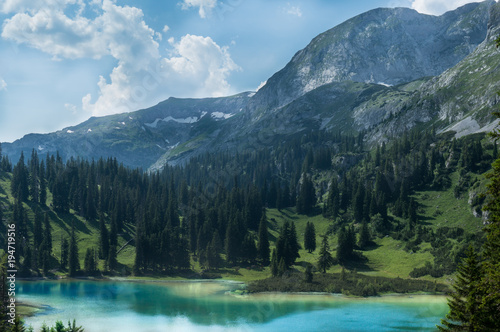 Fototapeta Naklejka Na Ścianę i Meble -  Amazing alpine scenery with vivid turquoise colored lake in foreground and pine forest covering a wonderful mountain meadow