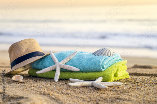 Sunglasses, towels, hat, sun block, shells and starfish on sandy beach