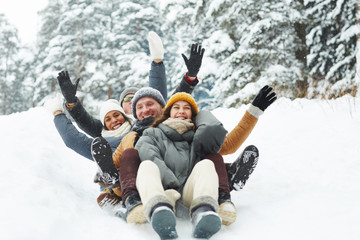 Four funny friends in winterwear riding down hill in snow on winter weekend