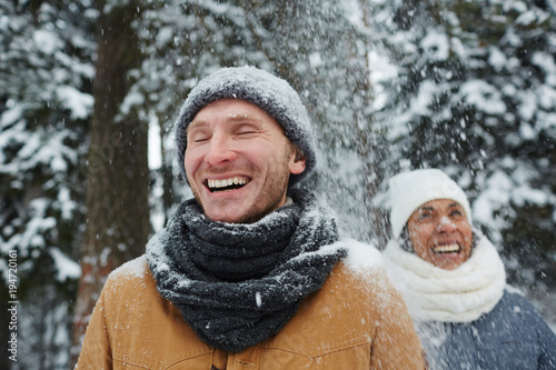 Laughing guy and his girlfriend enjoying snowfall during trip on winter day