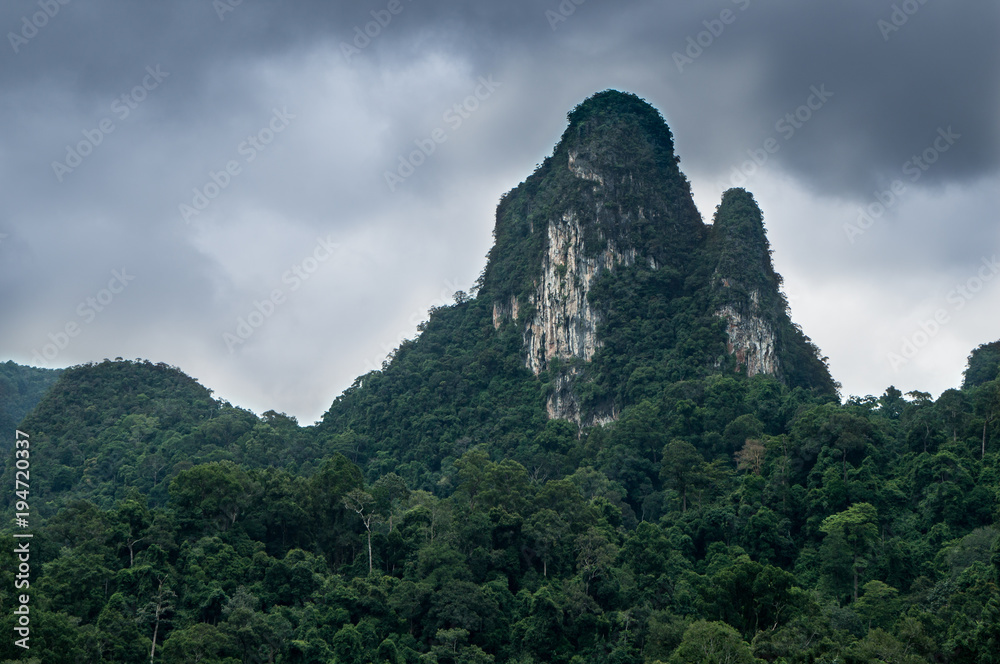 Imposing karst formation rising from the jungles of south east Asia and reaching towards a dramatic, cloudy sky