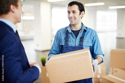 Delivery man with box talking to owner of new office area while carrying package