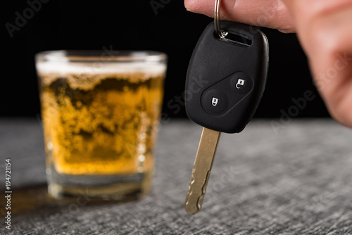 finger hold a car key in front of cup of beer concept of drunken driving