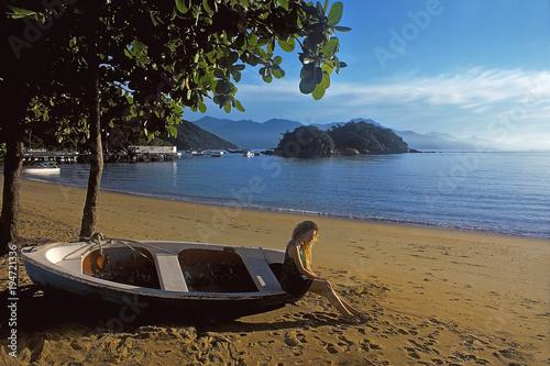 young blonde Woman sitting on beach near boat, Ilhagrande, Brazil photo