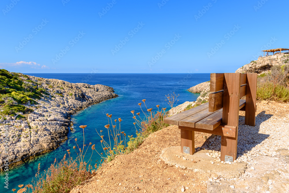 Bench on cliff with view of bay with crystal sea water. Korakonisi Island on western side of Zakynthos. Zante, Greece
