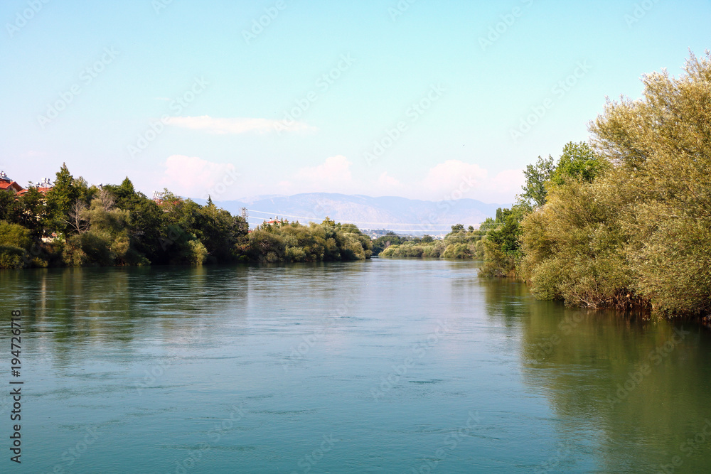 A small river flows calmly between its shores in sunny summer weather.