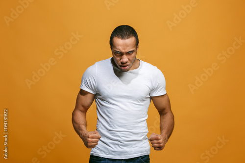 The young emotional angry man screaming on orange studio background