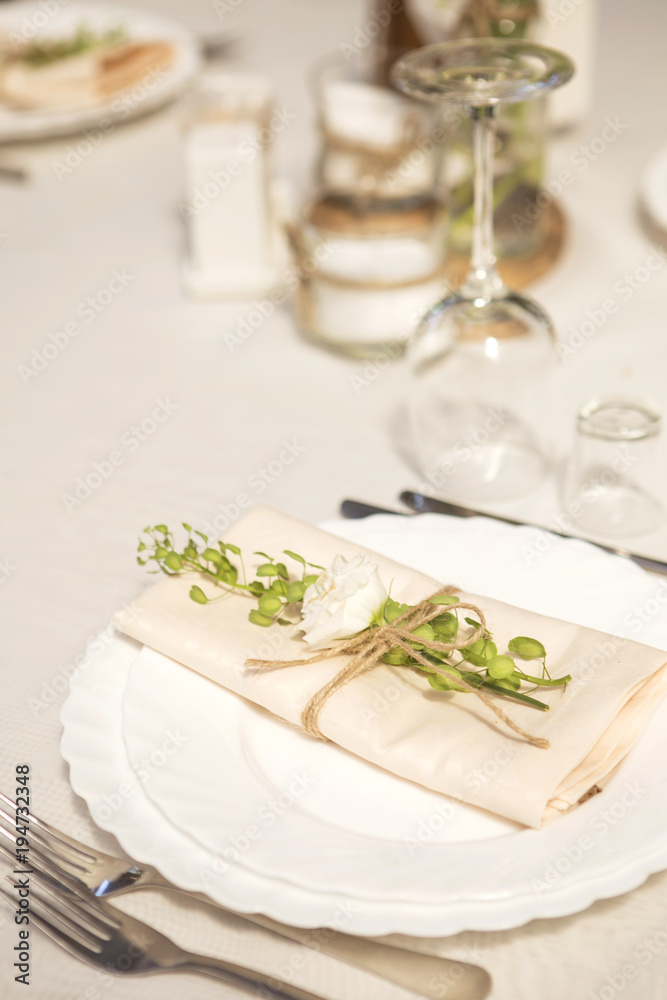 Simple but luxury rich table setting for a wedding celebration in nice cozy restaurant. Wineglasses, plates and bouquet of summer seasonal flowers on a table. Sunlight from a window. Copy space