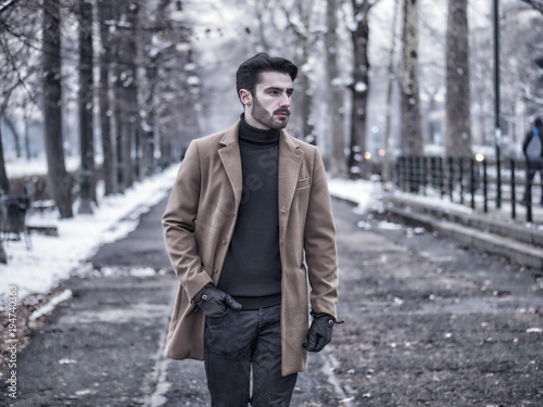 Handsome young man standing outside in winter, in snowy city. Cold urban setting